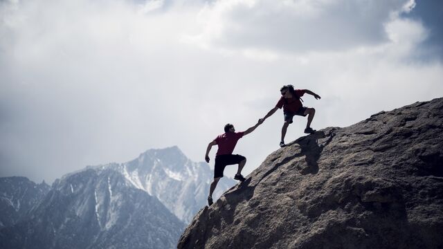 One climber helping another to the summit of a giant boulder SMALL